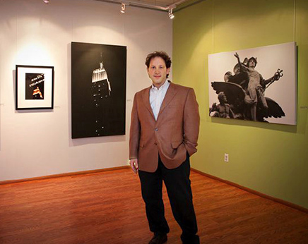 Andrew Darlow standing in front of a few of his prints during a solo show at Alfa Art Gallery